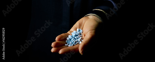 female hand isolated on black showing blue pills