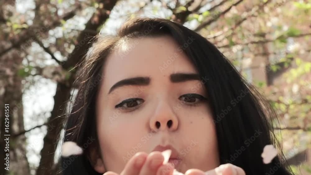 Playful Young Woman Blows A Handful Of Cherry Blossom Petals At Camera In Slow Motion