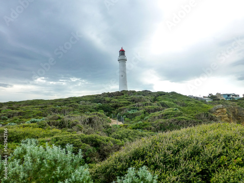 Lighthouse at the top of a green hill with a cloudy sky