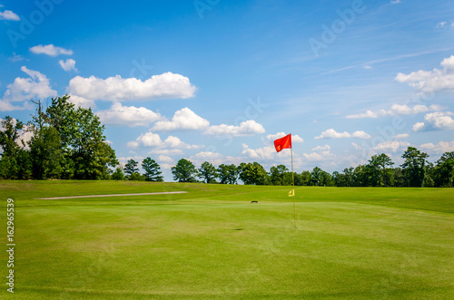 Golf course with beautiful green grass, bright blue skies and white puffy clouds. Recreational sporting activity of golf.