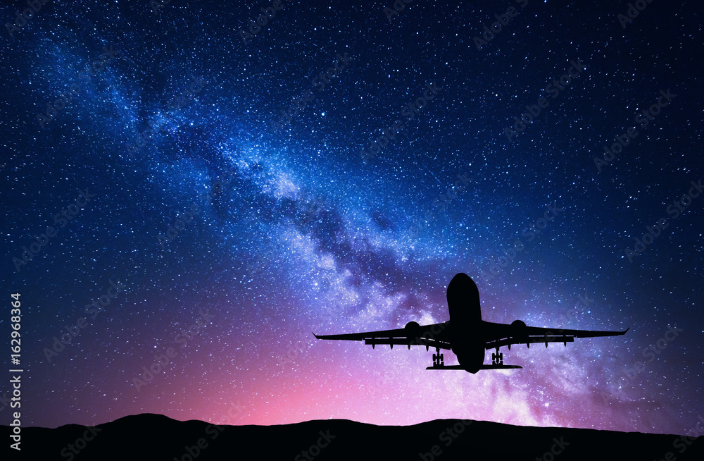 Naklejka premium Milky Way and silhouette of a airplane. Landscape with passenger airplane is flying in the starry sky at night. Space background. Landing airliner on the background of colorful Milky Way. Aircraft