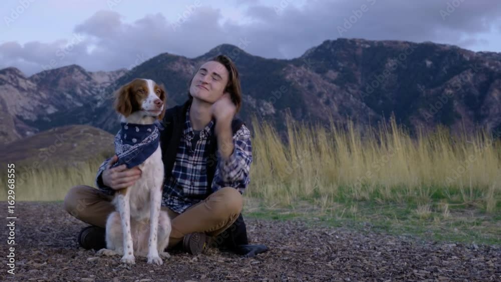 Adventurous Young Man Sits With His Dog And Watches The Sunset, He Pets Her Adventurous Young Man Sits With His Dog And Watches The Sunset, He Pets Her