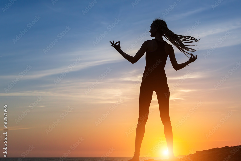 Silhouette of dancing girl against the sea during amazing sunset.
