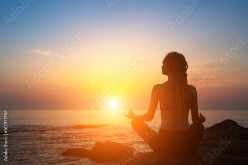 Yoga silhouette. Meditation girl on the ocean during beautiful sunset.