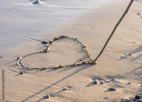 Heart being drawn in clean sand on the beach with stick