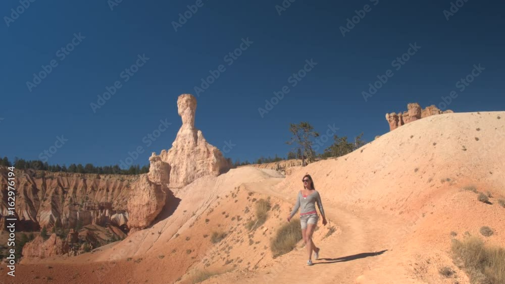 Young woman traveler walking along the winding path, exploring sandstone hoodoo formations in Bryce Canyon National Park in sunny Utah. Young woman tourist hiking the dusty trail in Bryce Canyon USA Young woman traveler walking along the winding path, exploring sandstone hoodoo formations in Bryce Canyon National Park in sunny Utah. Young woman tourist hiking the dusty trail in Bryce Canyon USA