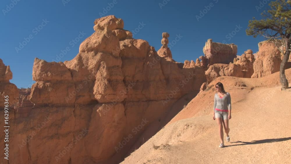 Young woman traveler walking along the empty path, exploring sandstone hoodoo formations in Bryce Canyon National Park in sunny Utah. Young woman tourist hiking the dusty trail in Bryce Canyon USA Young woman traveler walking along the empty path, exploring sandstone hoodoo formations in Bryce Canyon National Park in sunny Utah. Young woman tourist hiking the dusty trail in Bryce Canyon USA