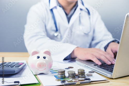 young medical doctor caucasian healthcare professional wearing a white coat with stethoscope in hospital,calculates on an electronic calculator laptop,medical fee concept,selective focus,vintage color photo