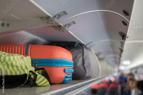 Foto Carry-on luggage on the top shelf over head on airplane, passenger put bag cabin