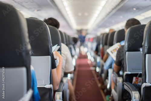 Fototapeta siedzenie pasażera, wnętrze samolotu z pasażerami siedzącymi na siedzeniach i stewardessa chodząca w przejściu w tle. Koncepcja podróży, kolor vintage