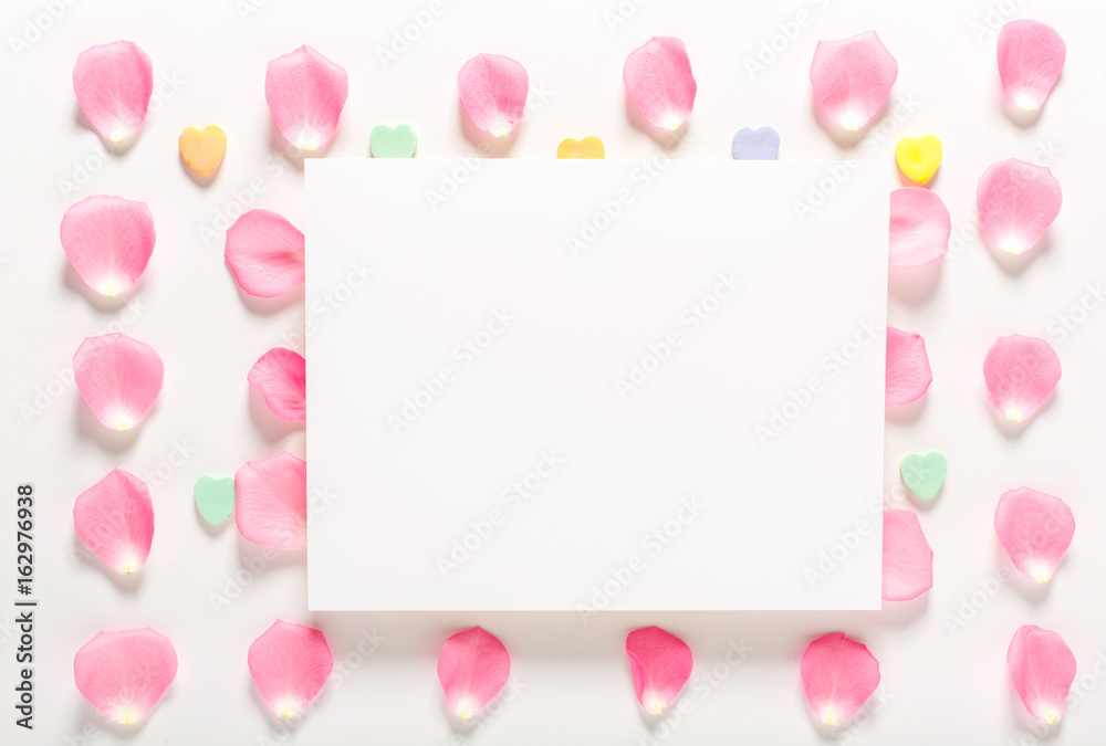 Rose petals and blank white message card aligned on a white background