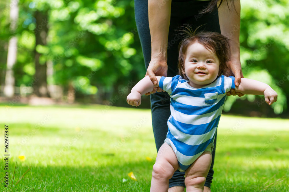 Baby boy learning to walk outside with the help of his parents Baby boy learning to walk outside with the help of his parents