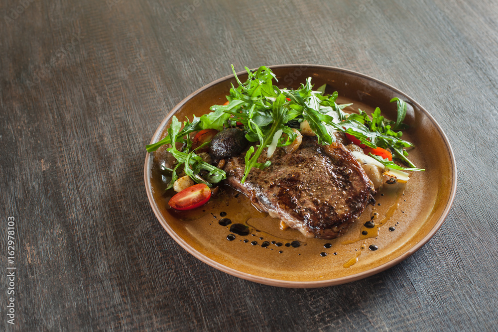 Beef steak with arugula and tomatoes on dark wooden background.
