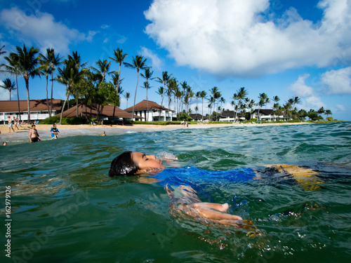 10 year old boy floating on back ain ocean at resort, Kiahuna Beach, Poipu Beach in front of Sheraton, Kauai, Hawaii, USA, sunny summer day