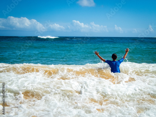 10 year old boy with arms up in victory or asking for help in surf, Kiahuna Beach, Poipu Beach in front of Sheraton, Kauai, Hawaii, USA, sunny summer day