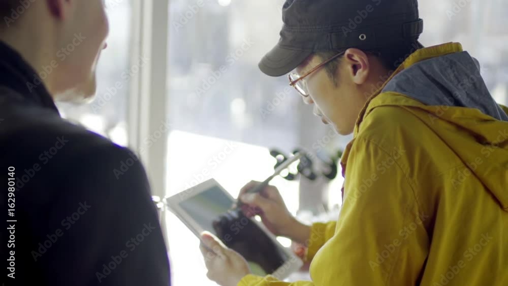 Multi-Ethnic Man Draws On A Tablet, His Boyfriend Points To The Screen Multi-Ethnic Man Draws On A Tablet, His Boyfriend Points To The Screen