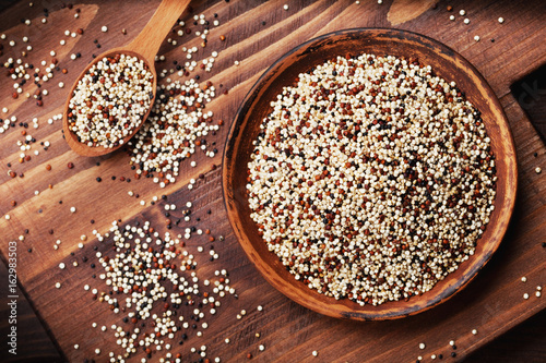 Mixed quinoa in bowl on wooden kitchen board top view.