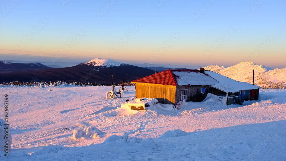 Vintage house on the top with snow.  Mountain view with a pine forrest on a sunset. Clear sky, winter