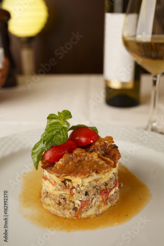 Moussaka arranged on a plate, Wine bottle and wineglass in background, Traditional dish in elegant setting, Selective focus with soft light