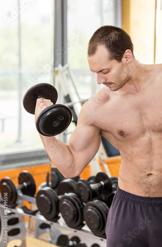 bodybuilder man doing biceps exercise with dumbbell in fitness club