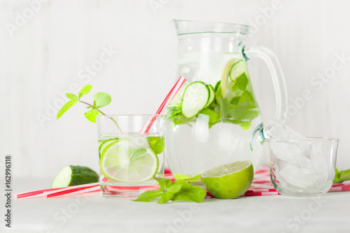 Detox water in a glass jug and a glass. Berries and lime, red and green. Fresh mint leaves.