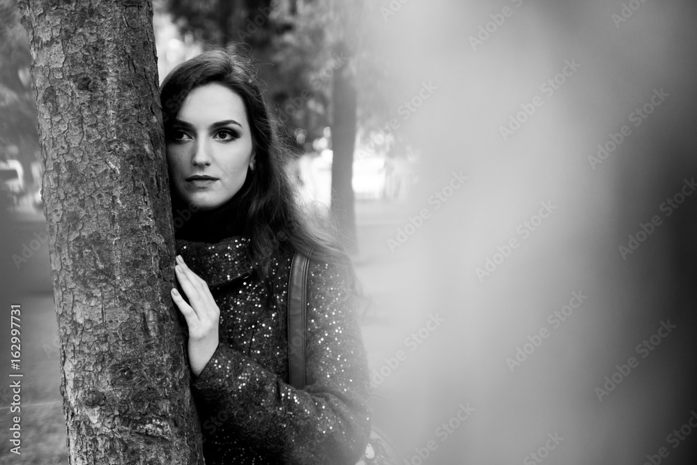 Pretty Brunette Standing near Tree in the Park. Black and White Portrait of Pretty Woman with Sensual Lips and Professional Makeup Outdoors.