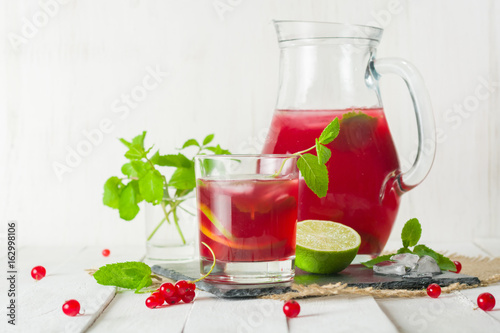 Compote in a glass jug and a glass. Berries and lime, red and green. Fresh mint leaves. Copy space.