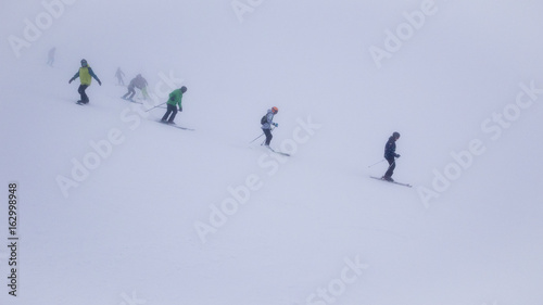 Skiers and snowboarders in thick fog on ski slope in ski resort.
