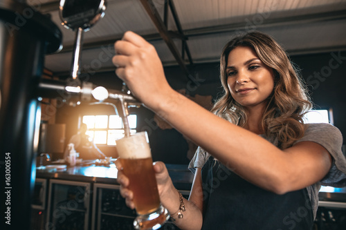 Beautiful female bartender tapping beer in bar