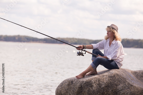 mature woman fisher sitting on sea rock