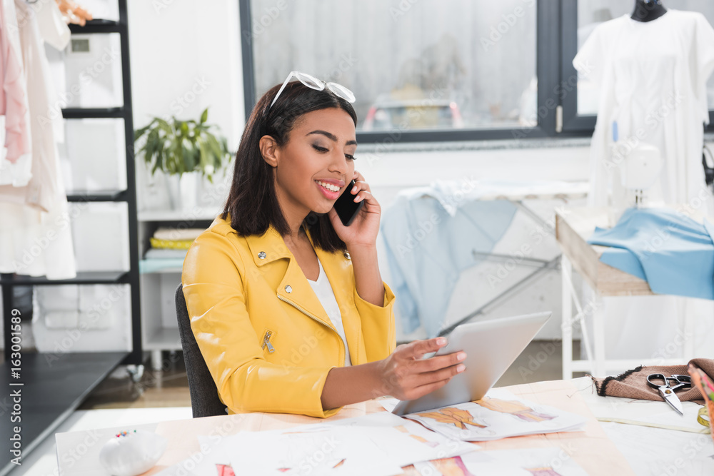 smiling woman talking on smartphone while using tablet at workplace smiling woman talking on smartphone while using tablet at workplace