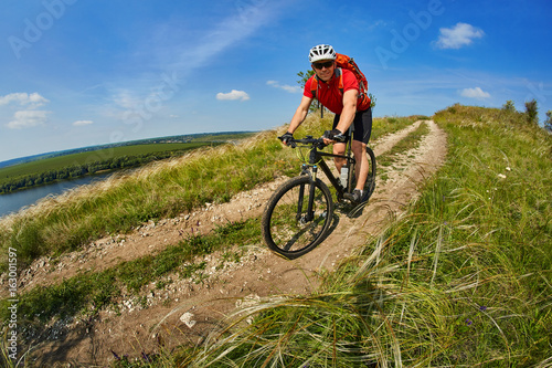 Young cyclist riding mountain bicycle through green meadow against beautiful sky.