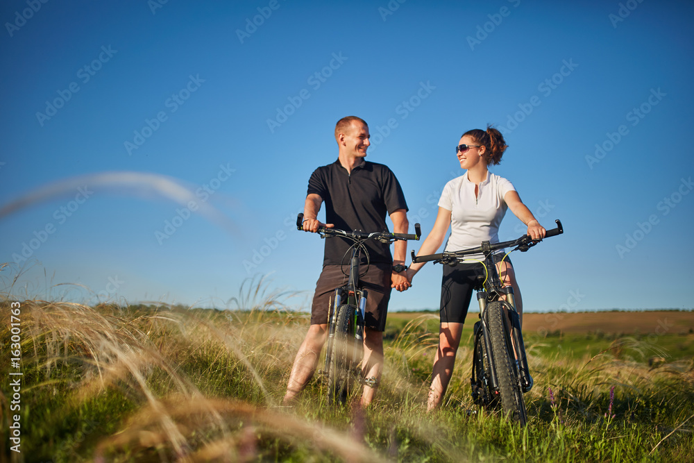 Couple of cyclists riding bicycles in meadow