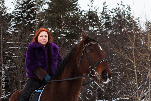 Woman with red hair and big horse outdoor in winter