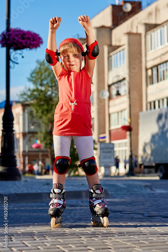 Pretty little girl in red t-shirt learning to roller skate outdoors on beautiful summer day