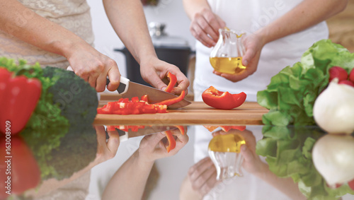 Close-up of four human hands are cooking in a kitchen. Friends having fun while preparing fresh salad. Vegetarian, healthy meal and friendship concept