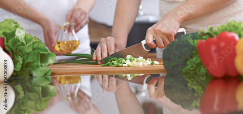 Close-up of four human hands are cooking in a kitchen. Friends having fun while preparing fresh salad. Vegetarian, healthy meal and friendship concept