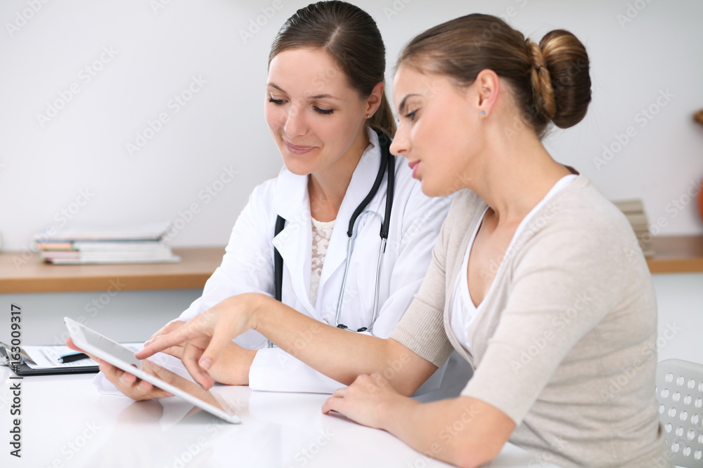 Doctor and patient sitting at the desk. Physician pointing into laptop computer. Medicine and health care concept Doctor and patient sitting at the desk. Physician pointing into laptop computer. Medicine and health care concept