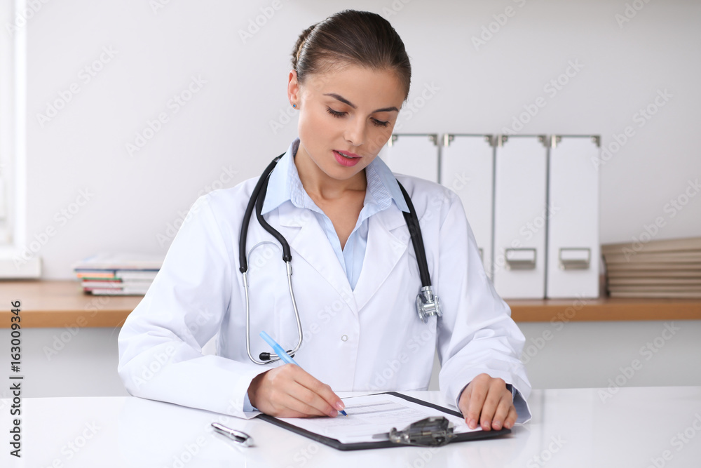 Doctor woman filling up medical form while sitting at the desk. Medicine and health care concept Doctor woman filling up medical form while sitting at the desk. Medicine and health care concept