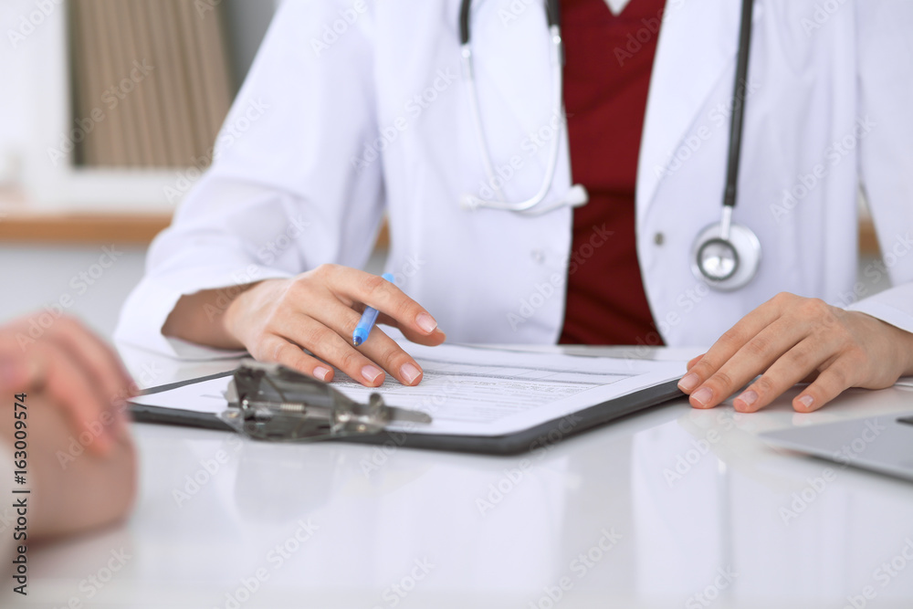 Close up of a female doctor filling up an application form while consulting patient Close up of a female doctor filling up an application form while consulting patient