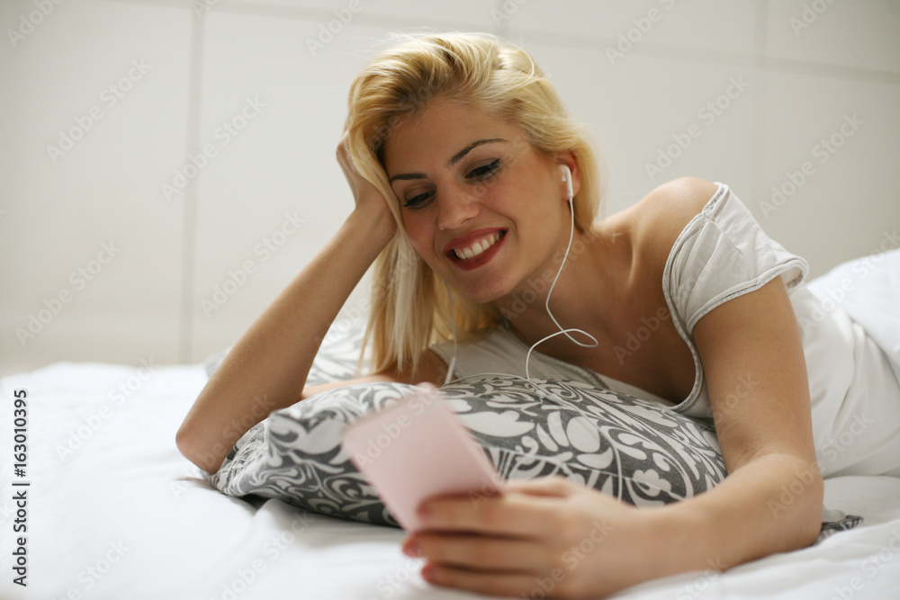 Φωτογραφία Woman listening to music on smart phone, and laying in bed.