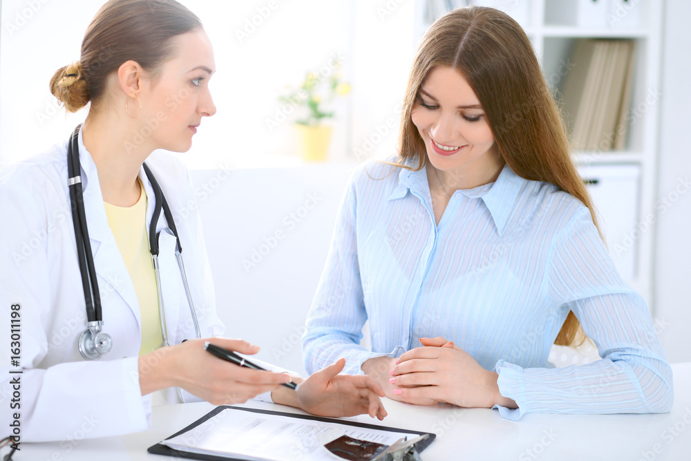 Doctor and patient have a talk while sitting at the desk near window Doctor and patient have a talk while sitting at the desk near window