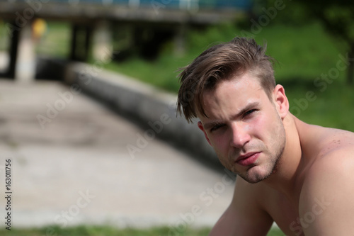 Man with concentrated face expression and naked torso sits outside