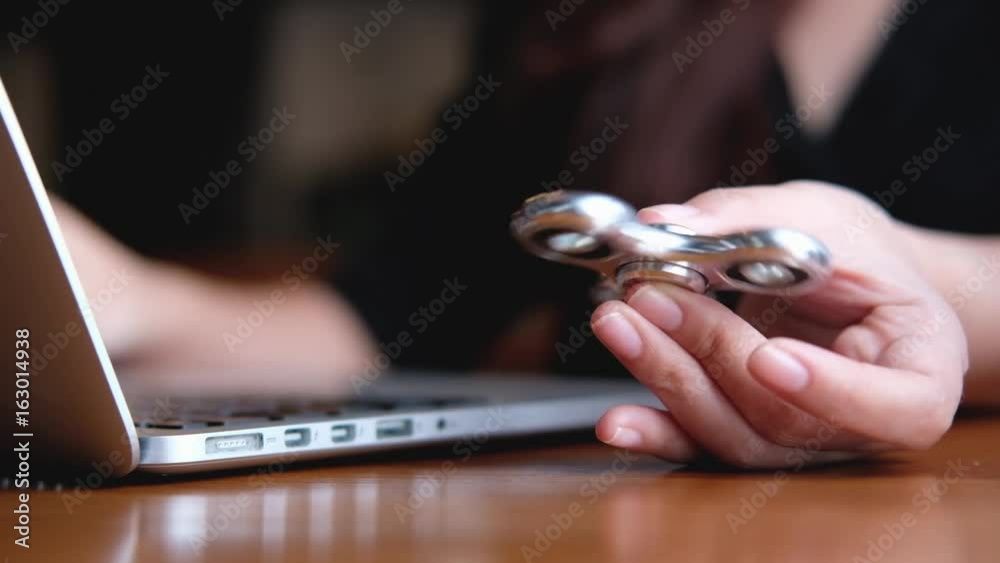 A woman using labtop while playing fidget spinner on vintage wooden table 