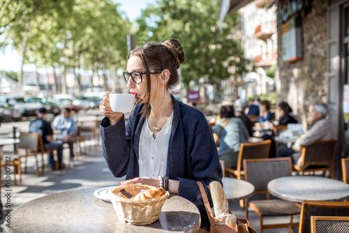 Photography Young woman having a breakfast with coffee and croissant sitting outdoors at the