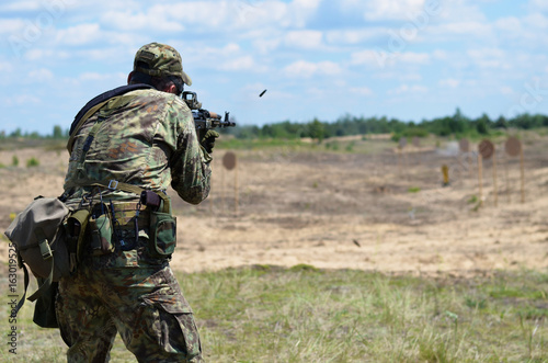 Soldier in camouflage with a Kalashnikov assault rifle  shooting in the field