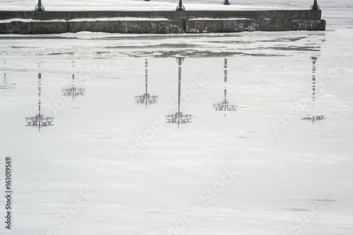 Reflection of the embankment with lanterns on the ice in the winter in the river in the early foggy morning