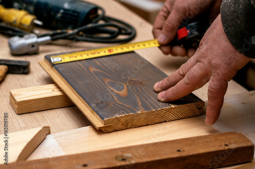 Craftsman measuring wooden plank with measuring tape