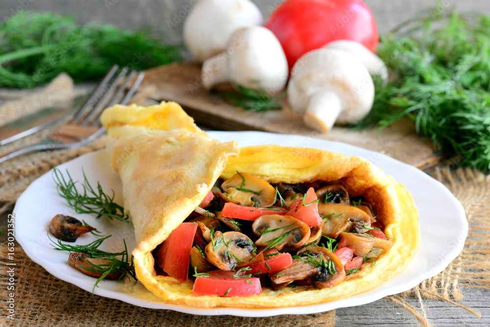 Ruddy omelet stuffed with fried mushrooms, fresh tomato slices and dill herbs. Home stuffed omelet on a plate. Rustic style Ruddy omelet stuffed with fried mushrooms, fresh tomato slices and dill herbs. Home stuffed omelet on a plate. Rustic style