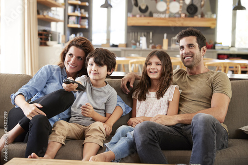 Family Sitting On Sofa In Open Plan Lounge Watching Television